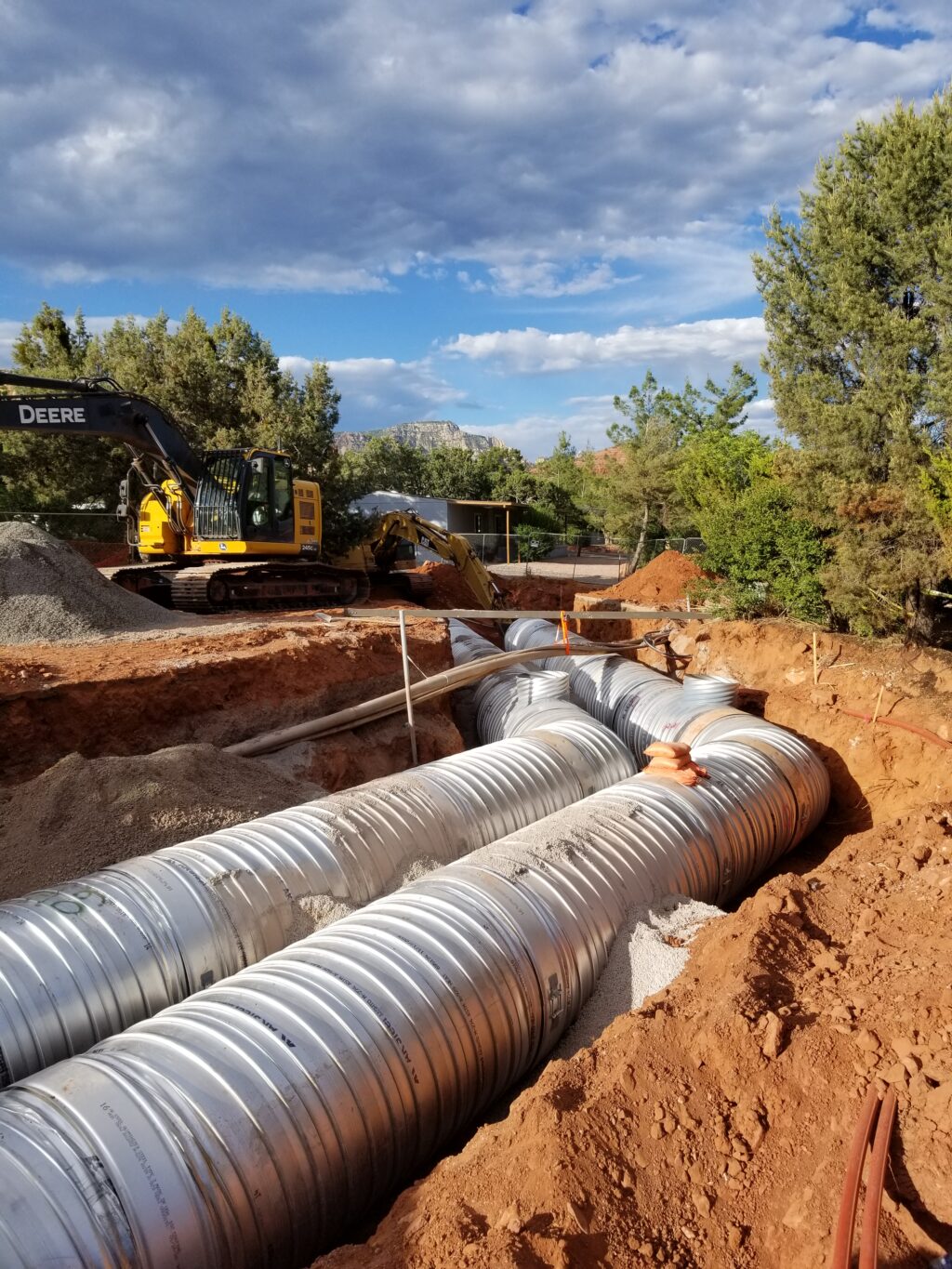 A view of large drainage pipes in a trench with construction equipment in the bacckground