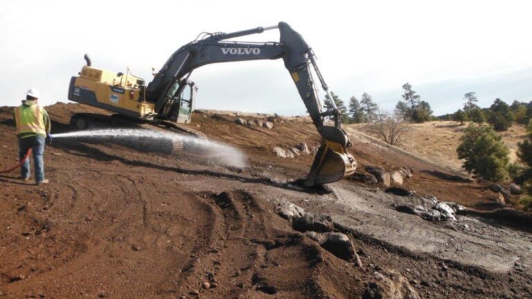 Construction worker spraying a hose next to a backhoe