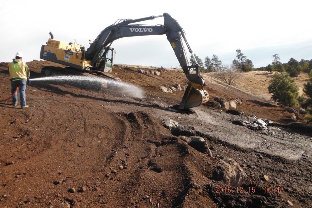 Construction worker spraying a hose next to a backhoe