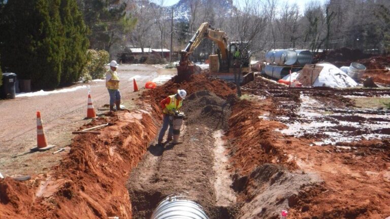 Construction workers filling in a trench with a large drainage pipe laid in