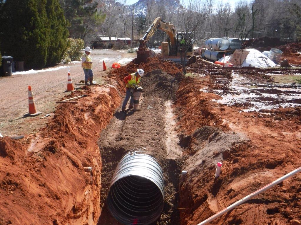 Construction workers filling in a trench with a large drainage pipe laid in