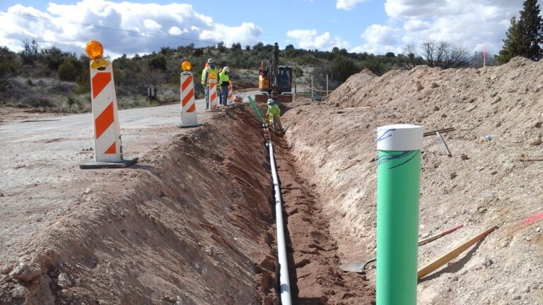 Construction workers with a backhoe digging a ditch for a water main