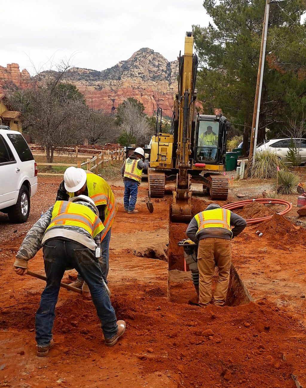 Construction workers with a backhoe digging a ditch in red earth in Sedona