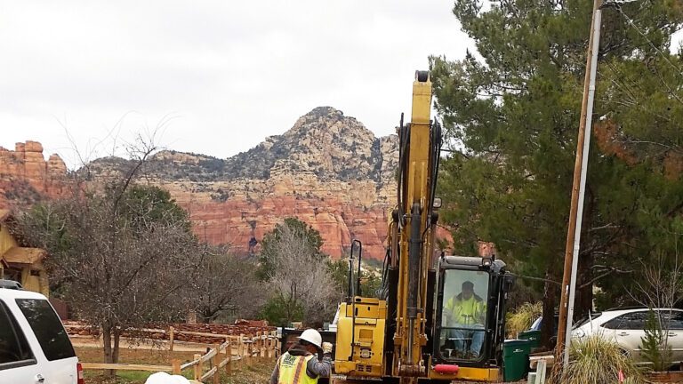 Construction workers with a backhoe digging a ditch in red earth in Sedona